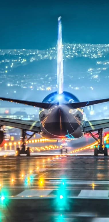 An aircraft on a runway at night against a hillside of city lights