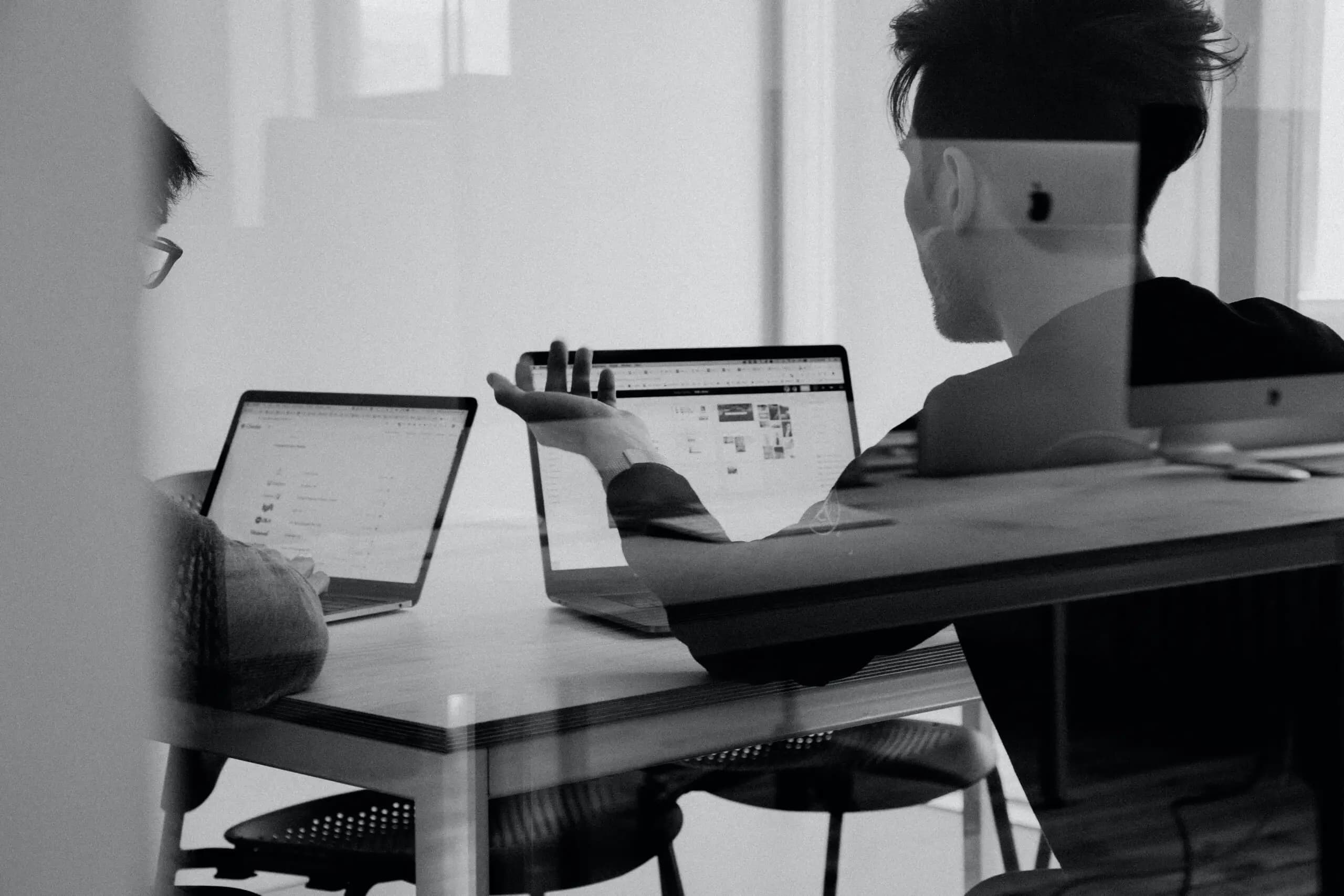 Two people reviewing work on laptops at a shared desk